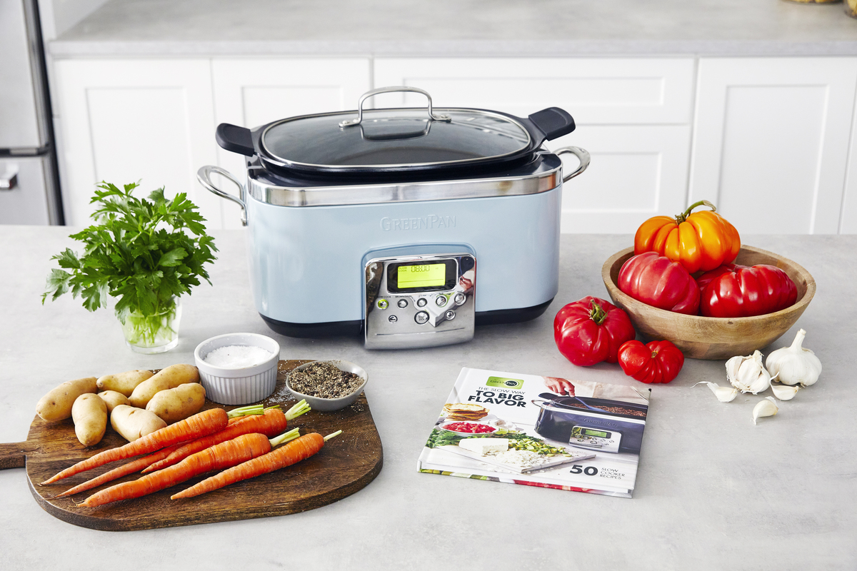 Image of the GreenPan Elite Slow Cooker in blue haze, surrounded by the cookbook and several fresh ingredients.