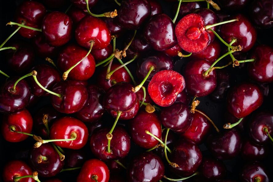 Close-up image of a pile of tart, deep red summer cherries, with a couple near the center bit in half.