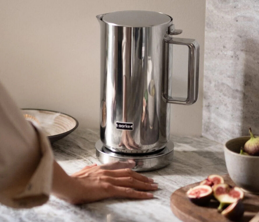 Image of an Aarke Stainless Steel electric kettle shown on a marble countertop with a hand reaching for it.