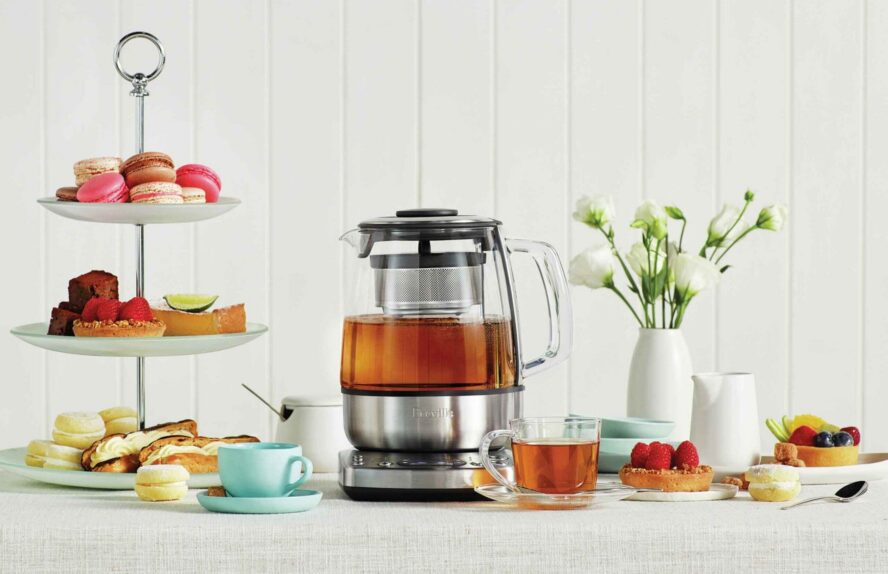 Image of the Breville Tea Maker shown on a table with other afternoon tea items like macarons and little cakes.