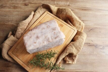 Image of a large block of beef tallow shown on a wooden cutting board next to a sprig of rosemary.