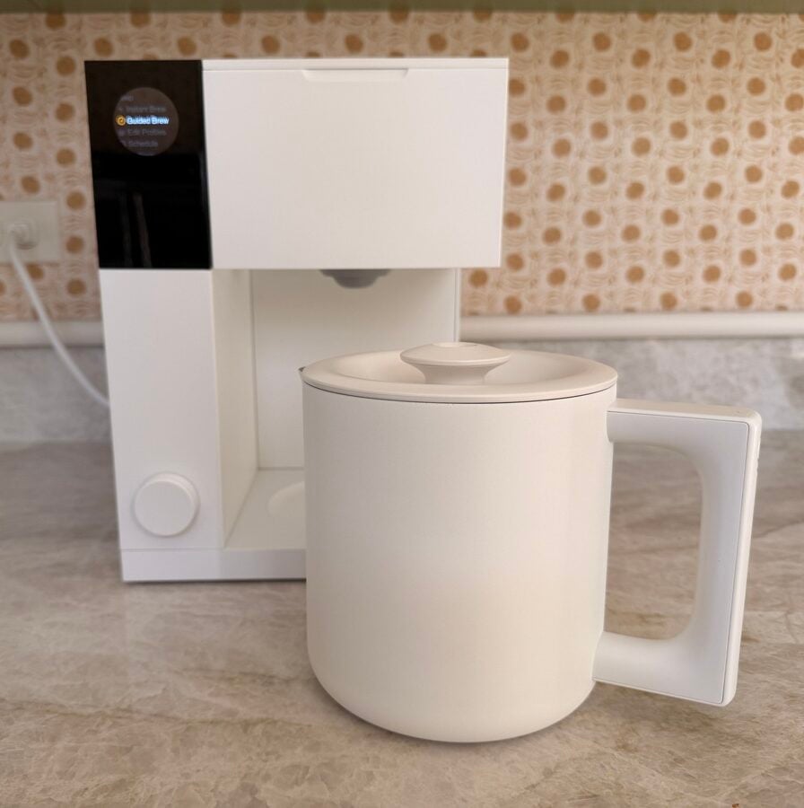 Image of the Fellow Aiden Precision Coffee Maker in white, with the carafe shown set in front of the appliance.