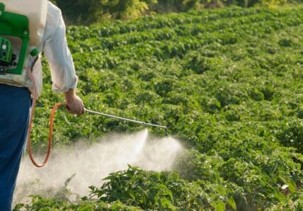 Image of a pesticide applicator spraying potentially cancer-causing pesticides on a field.