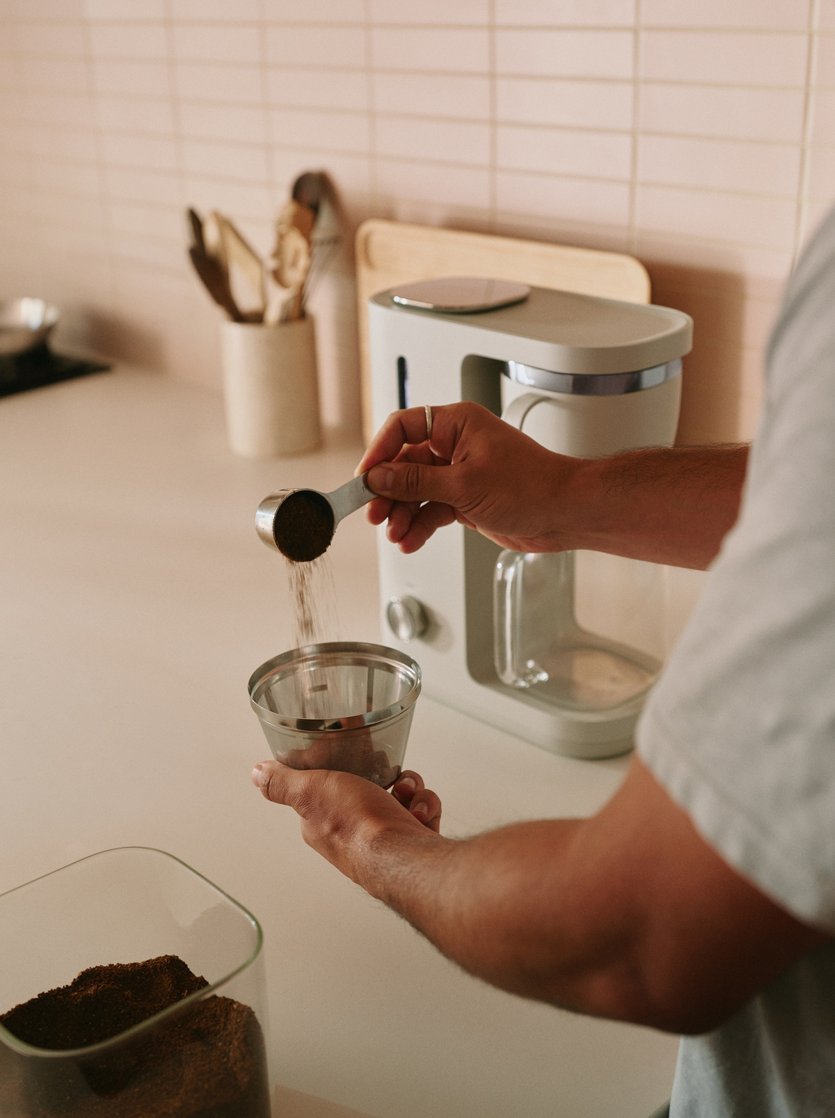 Image of a pair of hands using the Caraway Coffee Maker's included coffee scoop to put ground-up coffee beans into the reusable mesh filter.