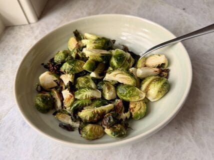 Image of a bowl of crispy air fryer Brussels sprouts, with a long spoon in the bowl for serving.