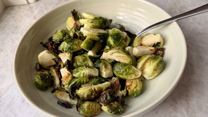 Image of a bowl of crispy air fryer Brussels sprouts, with a long spoon in the bowl for serving.
