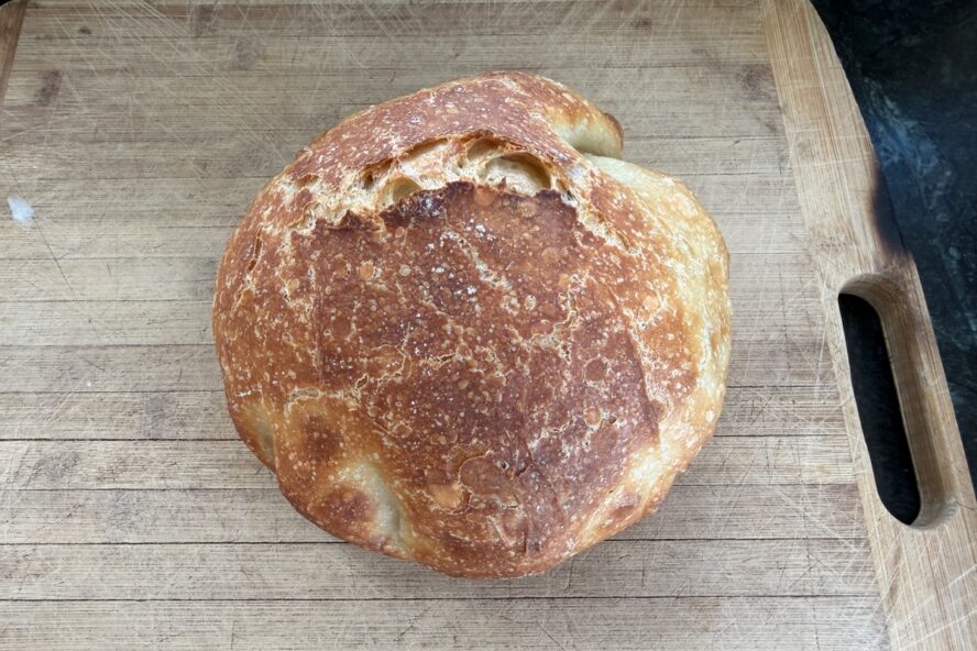 Image a gorgeous loaf of no-knead Dutch oven bread shown on a wooden cutting board.