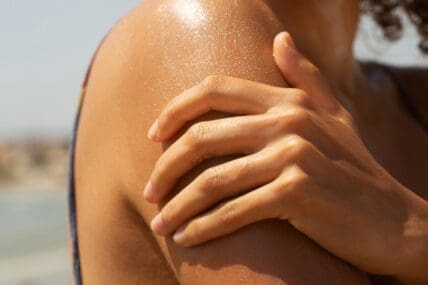 dewy hydrated summer skin, zoomed in on a hand holding a bare shoulder