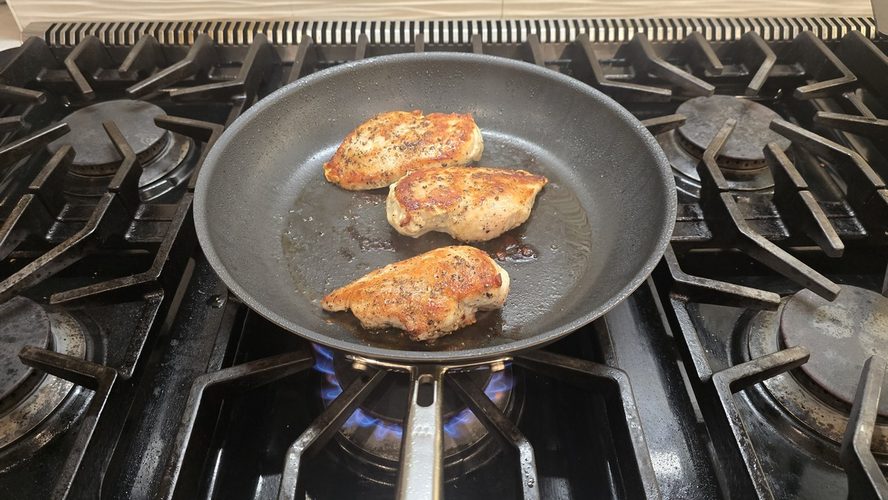 Image of three seared chicken thighs shown in a Misen Carbon Nonstick frying pan.