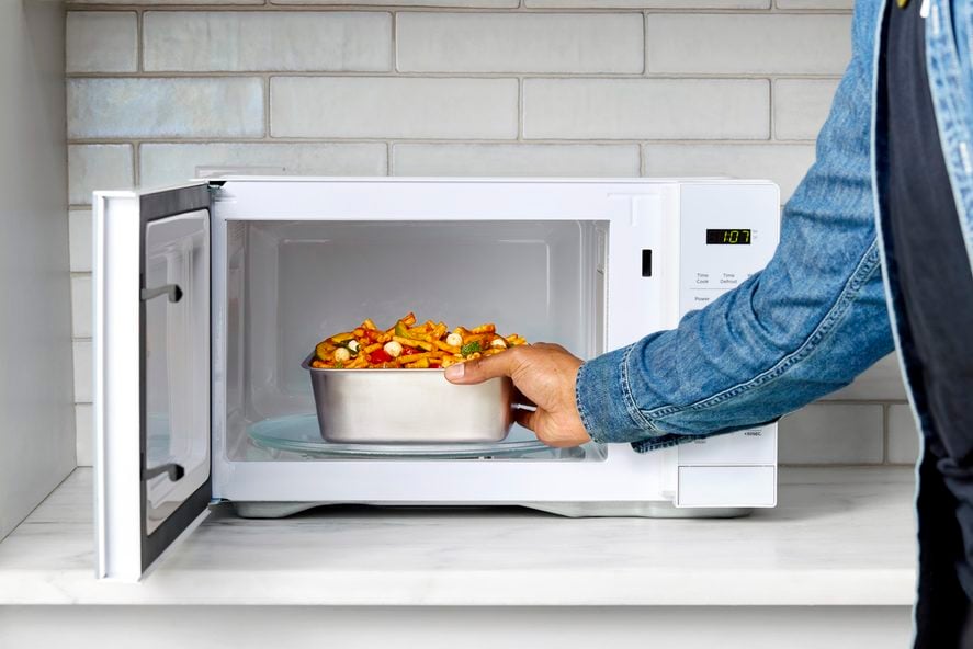 Image of an open microwave with a hand reaching in and placing a Misenware stainless steel food storage container inside.