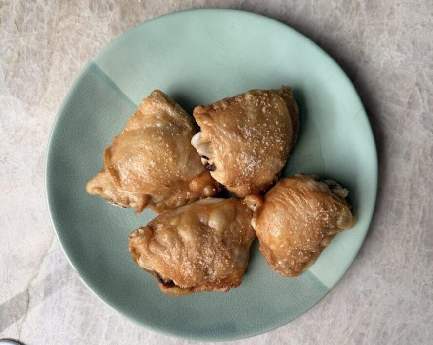 Overhead shot of four air fryer chicken thighs with crispy skin on a plate.