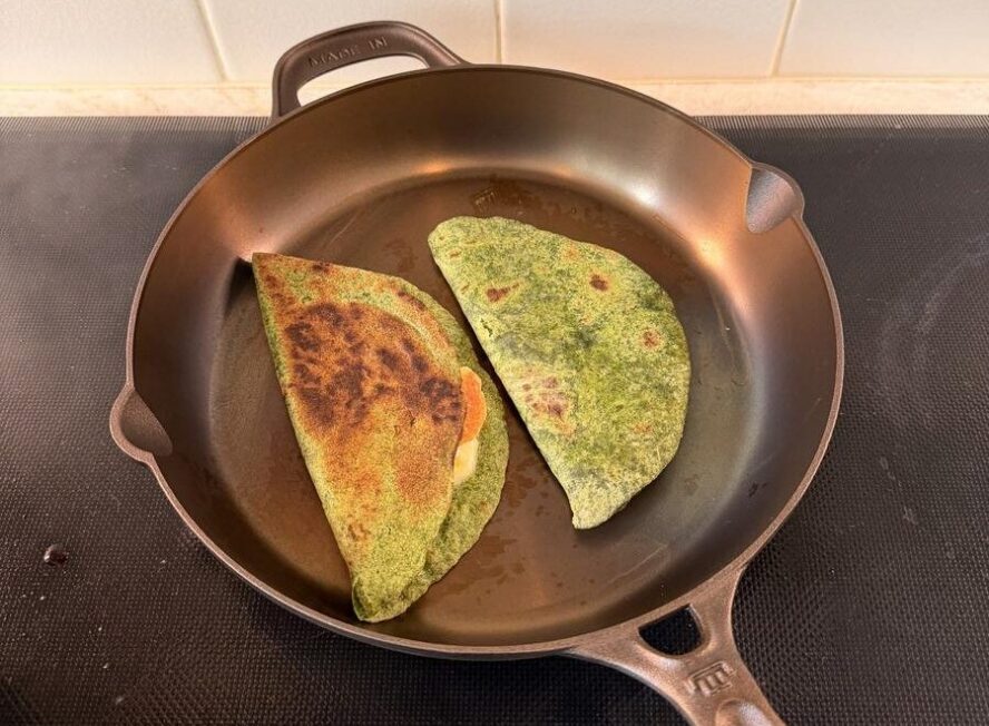 Image of a Made In cast iron skillet on an induction stovetop with two quesadillas in the skillet.