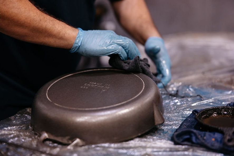 Image of a pair of gloved hands handling a Made In cast iron skillet at the foundry where they are made.