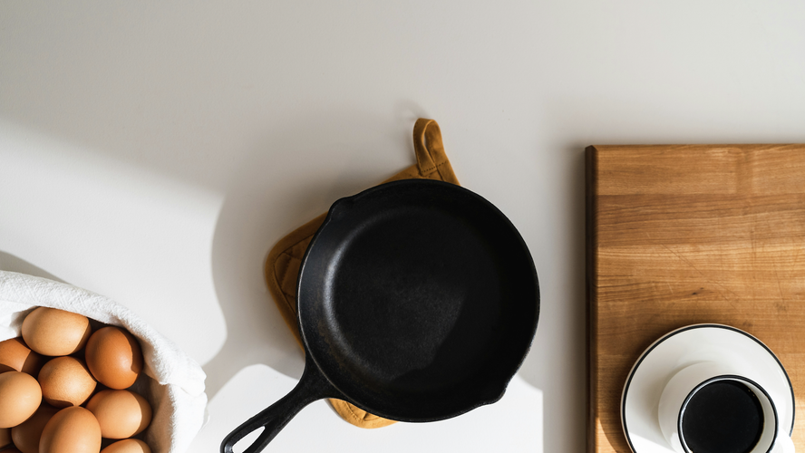 overhead shot of a well-seasoned cast iron skillet with a bowl of eggs and a cup of black coffee in a white mug on a white saucer