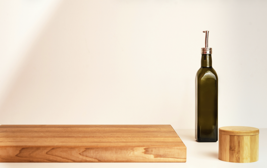 wood cutting board on a counter with a wood salt container and single glass refillable oil bottle with pour spout