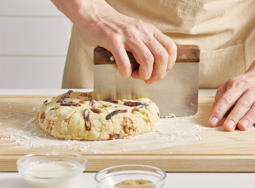 Image of the Misen Bench Scraper being used to slice bread dough on a butcher block.