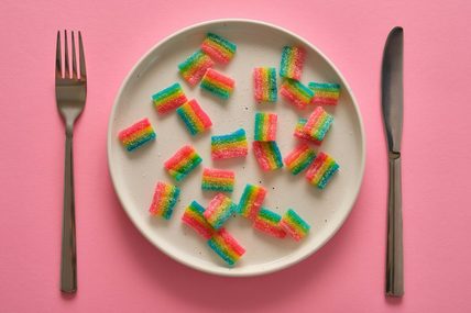 Image of a plate of sour candies with a knife and fork set beside the plate, all shown on a pink background.