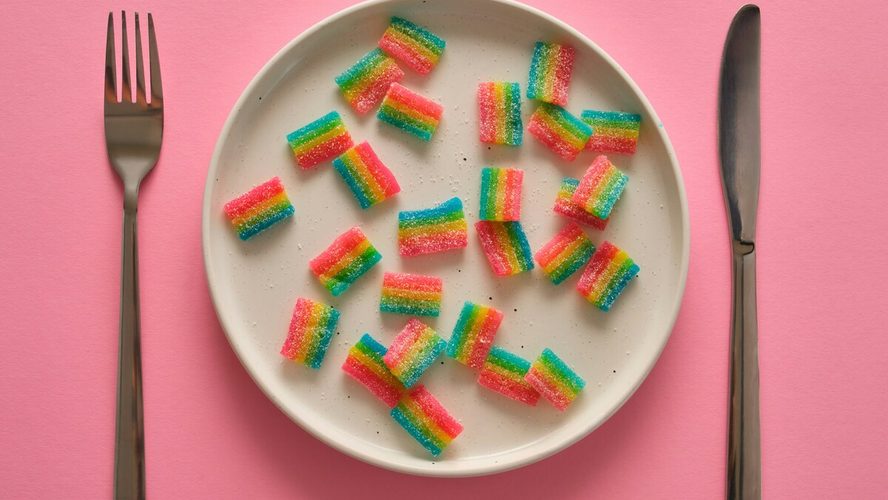 Image of a plate of sour candies with a knife and fork set beside the plate, all shown on a pink background.